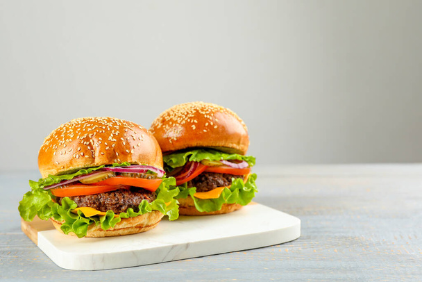 Tasty burgers on light grey wooden table, space for text. Fast food - 写真・画像