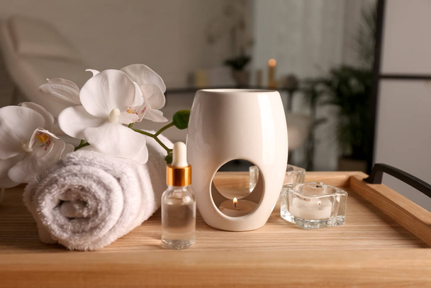 Lâmpada de aroma, garrafa de óleo, toalha enrolada e velas em bandeja de madeira dentro de casa - Foto, Imagem