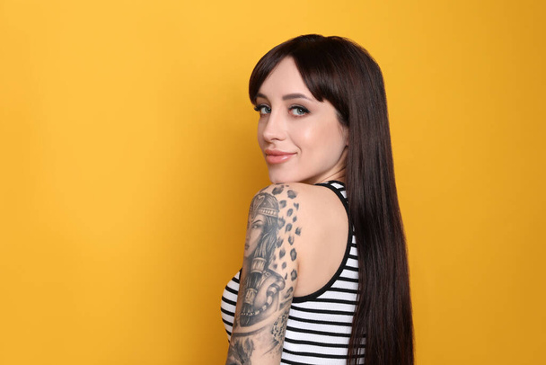 Beautiful woman with tattoos on arm against yellow background. Space for text - Foto, Imagen