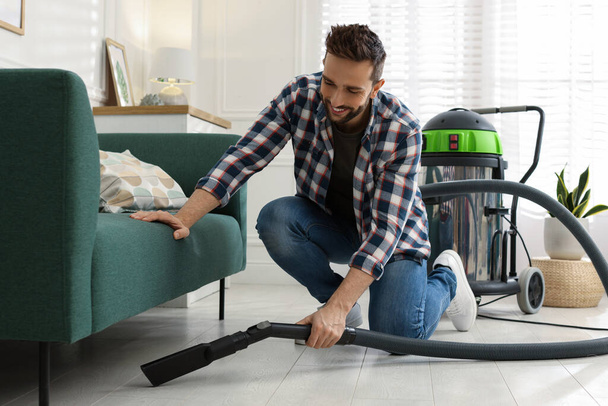 Man vacuuming floor under sofa in living room - Fotó, kép