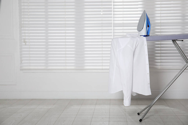 Modern iron and clean shirt on board indoors, space for text - Photo, image