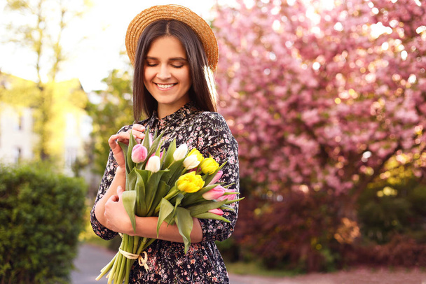 Mooie jonge vrouw met boeket tulpen in park op zonnige dag, ruimte voor tekst - Foto, afbeelding