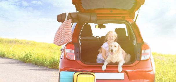 Cute little girl and her dog in open car trunk outdoors. Space for text - Fotoğraf, Görsel