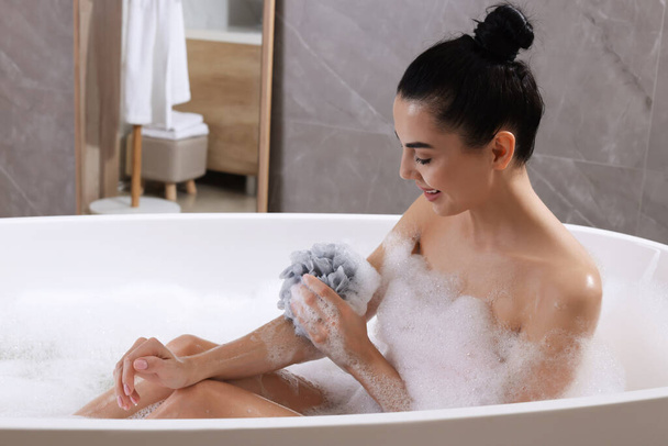 Woman taking bath with mesh pouf indoors - 写真・画像