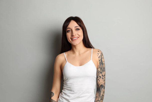 Beautiful woman with tattoos on arms against grey background - Foto, Imagem