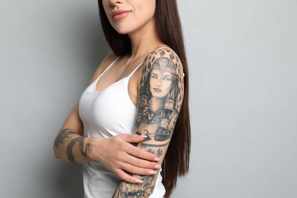 Beautiful woman with tattoos on arms against grey background, closeup - Foto, afbeelding