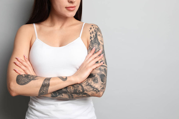 Beautiful woman with tattoos on arms against grey background, closeup. Space for text - 写真・画像