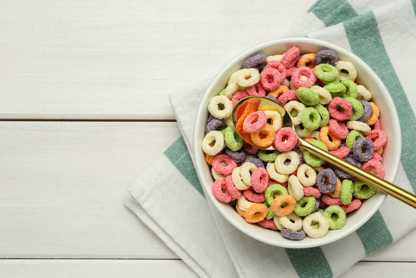 Bowl of sweet crispy corn rings on white wooden table, flat lay with space for text. Breakfast cereal - Φωτογραφία, εικόνα