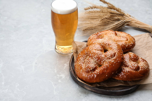 Tasty pretzels, glass of beer and wheat spikes on light grey table, space for text - Photo, image