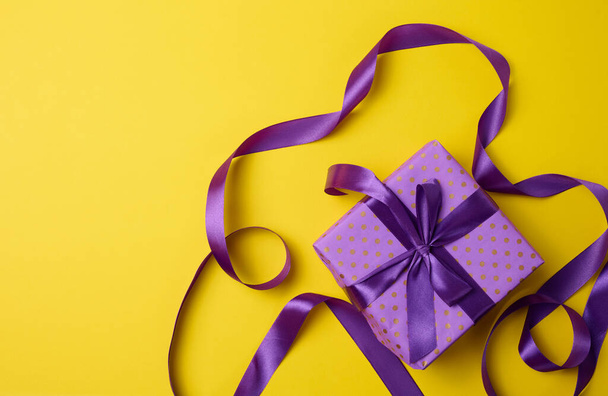 cajas envueltas en papel púrpura regalo y cinta de seda sobre un fondo amarillo, vista superior. Felicitaciones y sorpresa - Foto, imagen