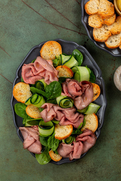 Biftekli et ve sebze salatası, sarımsaklı ekmek, ıspanak ve salatalık. Yeşil Tablo yüzeyi, üst görünüm, dikey görüntü. - Fotoğraf, Görsel