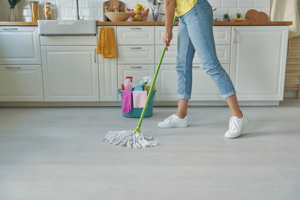 Close-up of woman cleaning floor with mop while standing at the domestic kitchen - Zdjęcie, obraz