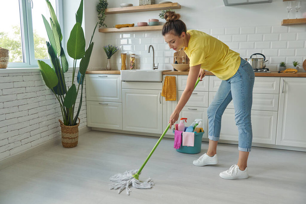 Full length of beautiful young woman cleaning floor with mop while standing at the kitchen - Fotoğraf, Görsel