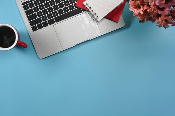 Laptop von oben, Kaffeetasse, Notizbuch und Blumentopf auf blauem Hintergrund. - Foto, Bild