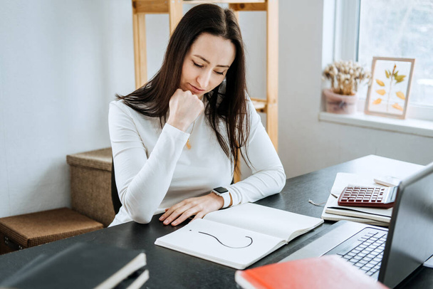 Accounting Questions and Answers, How to Solve Accounting Problems. Female Accountant looking to question mark in a notepad on the background of laptop and calculator - Photo, Image