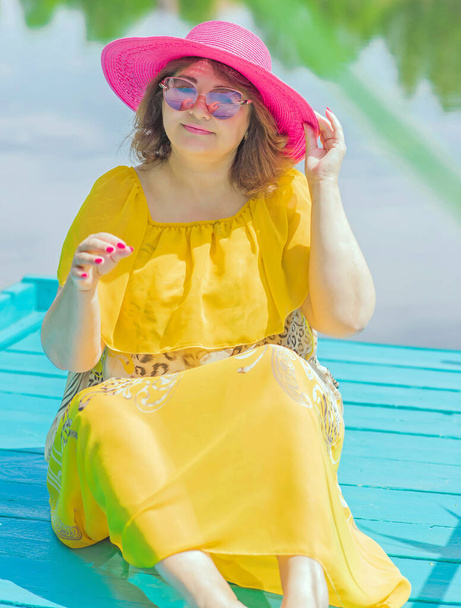 Plus size European or American woman at nature in yellow romantic dress and pink hat, enjoy the holidays. Life of people xl size, happy nice natural beauty woman. Concept of overweight - Valokuva, kuva