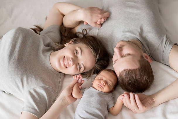 Pasgeboren baby in de armen van moeder en vader op bed. Briefkaart Moeder- en vaderdag. Dag van de kinderbescherming. Wereldgeluksdag. Een lachend kind. Gelukkig ouderschap. - Foto, afbeelding