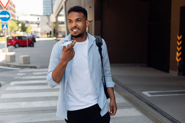 Красивий афроамериканський хлопець записує голосове повідомлення на мобільний телефон, чорний чоловік використовує віртуального помічника по телефону під час прогулянки по міській вулиці, копіює простір
 - Фото, зображення