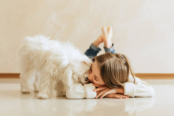 lány 9 éves hosszú haj modell egy kisállat kutya Máltai iskolás lány otthon életmód egy bézs háttér allergia állatorvos - Fotó, kép
