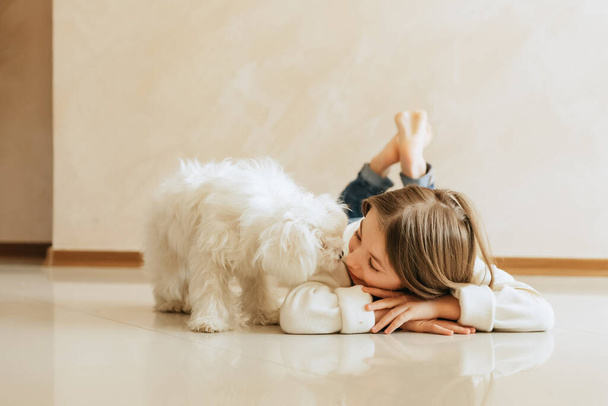 girl 9 years old with long hair model with a pet dog Maltese schoolgirl at home lifestyle on a beige background allergy veterinarian - Foto, afbeelding