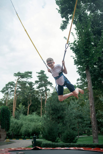 Poika roikkuu silmukoissa, hyppää korkealle trampoliinilla huvipuistossa. Viikonloppu teemapuistossa. Teini pitää hauskaa. - Valokuva, kuva