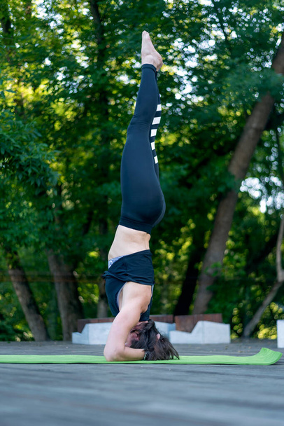 Een atletische jonge vrouw staat op haar hoofd. Meisje oefent yoga in de pose van Shirshasana - Foto, afbeelding