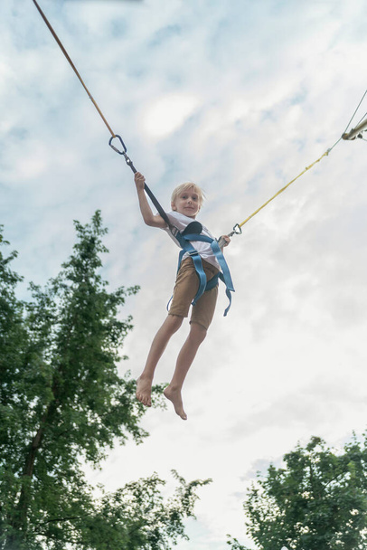 Boy rides trampoline in an amusement park and jumps high into sky. Child has fun in the theme park - Fotografie, Obrázek