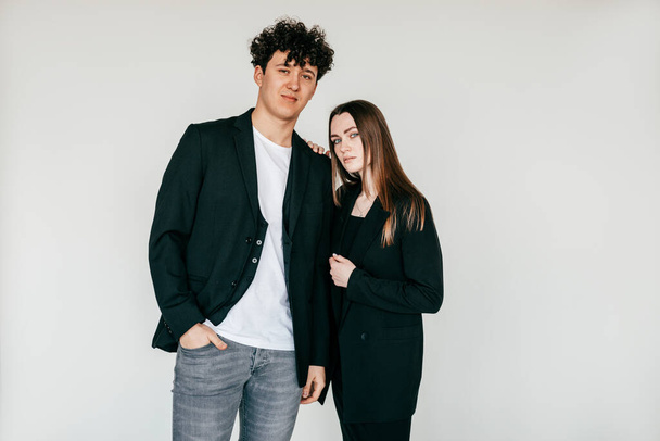Portrait of young attractive dark-haired curly man and long haired woman in black outfit, sanding close. Female touching shoulder, bound and love relationship couple. Studio shot on white background. - Zdjęcie, obraz