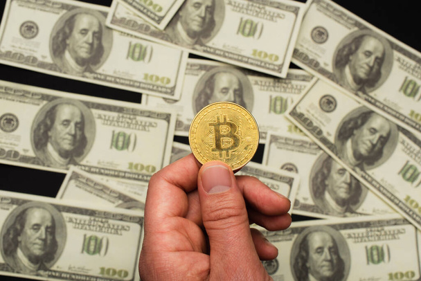 KYIV, UKRAINE - APRIL 26, 2022: Cropped view of man holding bitcoin near blurred dollars on black background - Photo, image