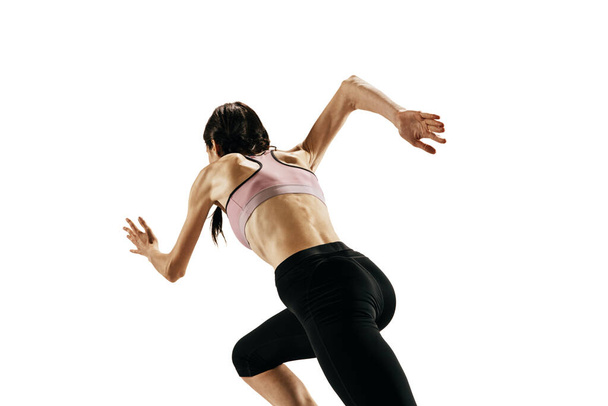Rear view of young caucasian woman running isolated on white studio background. One female runner or jogger. Sport, track-and-field athletics, competition concept. Copy space for ad, text - 写真・画像