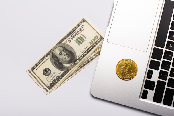 KYIV, UKRAINE - APRIL 26, 2022: Top view of dollars near bitcoin on laptop on white background - Фото, изображение