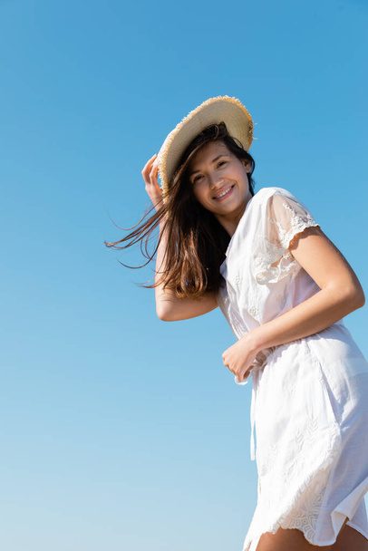 Low angle view of positive woman in dress holding straw hat with sky at background  - Foto, Imagem