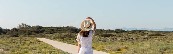 Вид сзади женщины в соломенной шляпе идущей по тропинке по пляжу, баннер  - Фото, изображение