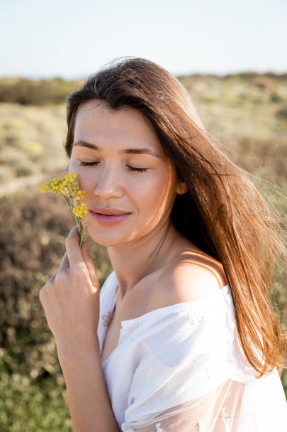 Портрет жінки закриває очі і тримає квіти біля щоки на пляжі
  - Фото, зображення