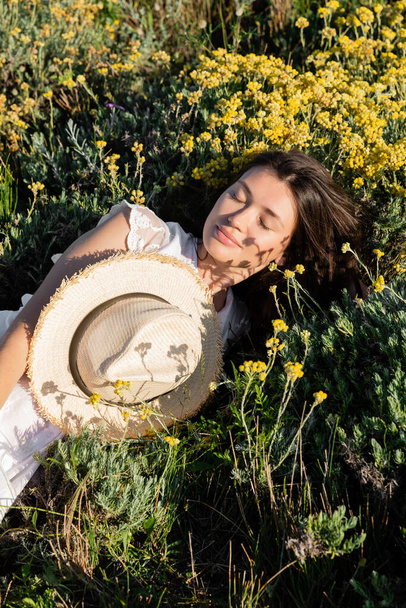 Femme brune couchée près du chapeau de soleil et des fleurs sur la prairie  - Photo, image