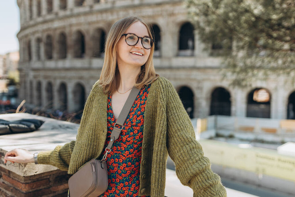Portret van een vrolijke vrolijke vrouw op de achtergrond van Colosseum in Rome, Italië. Mooie glimlachende vrouw in jurk buiten. Concept stedelijke levensstijl. - Foto, afbeelding