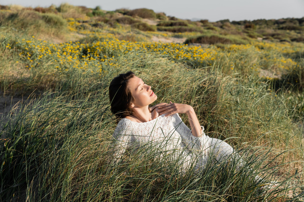 Woman in summer dress relaxing on grass on beach  - 写真・画像