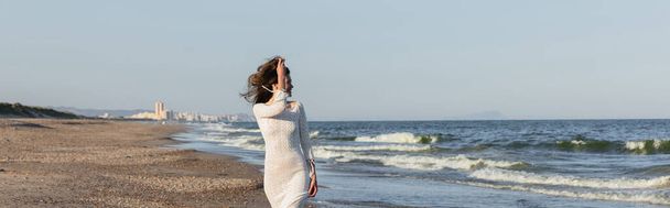 Side view of cheerful young woman in knitted dress looking at sea, banner  - Foto, Imagem