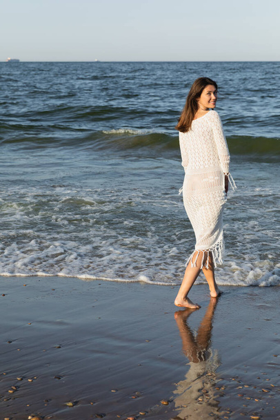 Pretty woman looking at camera while walking near sea on beach  - Fotó, kép