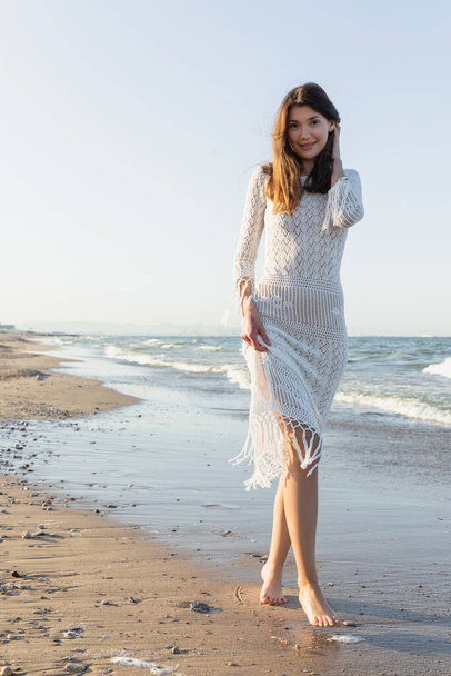 Pretty young woman looking at camera on beach with sea at background  - 写真・画像