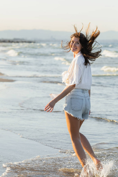 Позитивная женщина в рубашке смотрит в камеру на морском побережье  - Фото, изображение