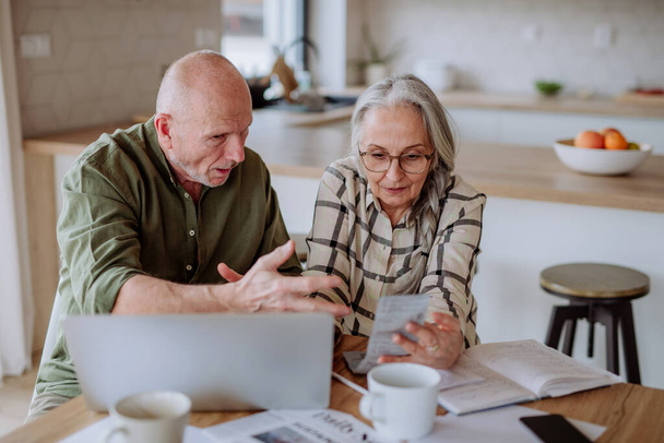 A stressed and sad senior couple calculate expenses or planning budget together at home. - Photo, Image