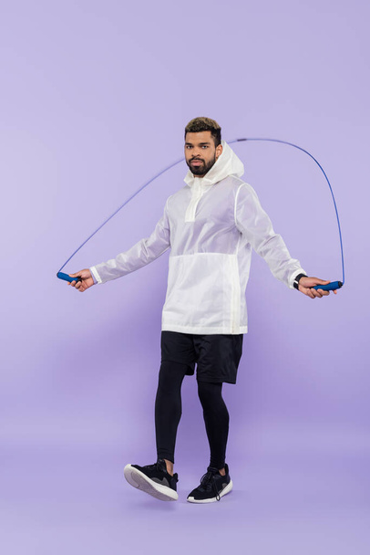 full length of young african american sportsman in sportswear exercising with skipping rope on purple - Photo, Image
