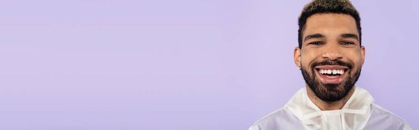 portrait of happy african american man smiling and looking at camera isolated on purple, banner - Foto, Imagen