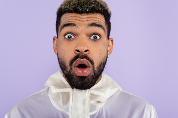 portrait of shocked african american man with blue eyes isolated on purple  - Fotó, kép