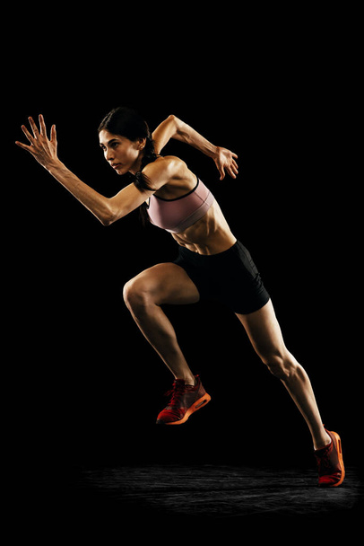 Achievements and challenges. Young muscular woman running isolated on black background. Sport, track-and-field athletics, competition and active lifestyle concept. Copy space for ad, text - Foto, Bild