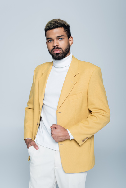 stylish african american man in yellow blazer posing with hand in pocket isolated on grey - Foto, afbeelding