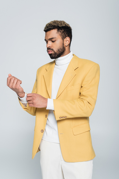 stylish african american man in yellow blazer adjusting sleeve isolated on grey  - Foto, Imagen