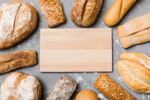 自家製パンの種類の背景にミニマリスト木製のまな板ブランクモックアップ.背景としての新鮮なパンのさまざまな種類,あなたのテキストやデザインのためのスペースとトップビュー. - 写真・画像