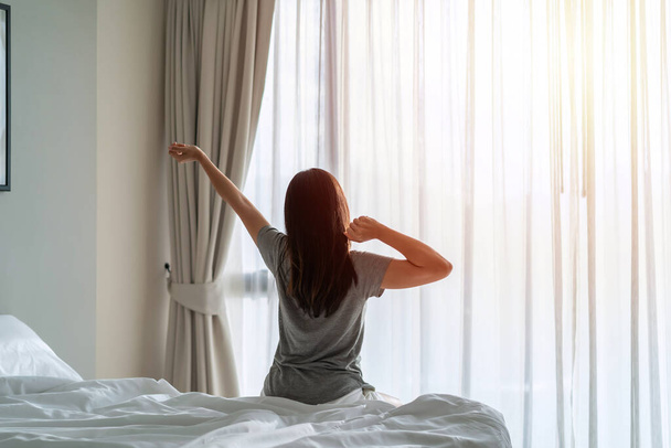 Young asian woman sitting on the bed and stretch oneself in the morning at home - Φωτογραφία, εικόνα